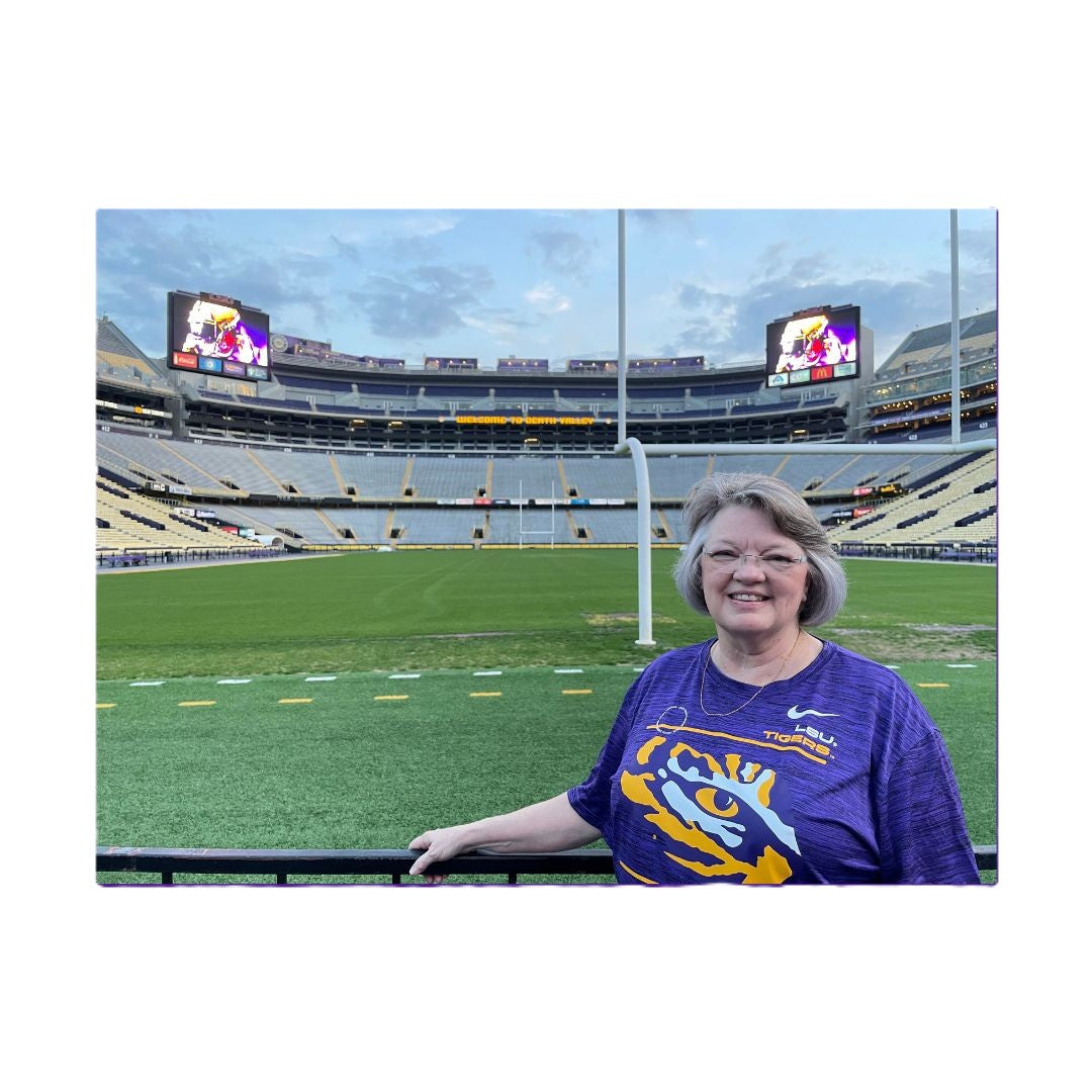 Beautiful Christian woman in a purple LSU Tiger shirt standing on the LSU Death Valley football field with the LSU Tigers stadium in the background
