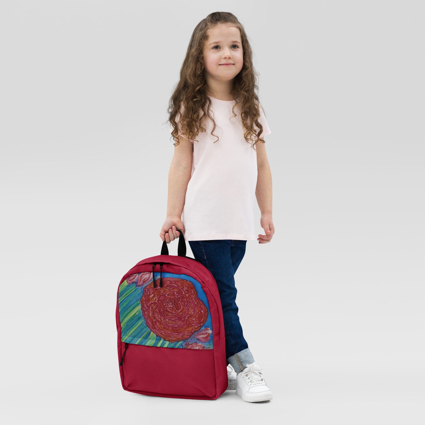Young girl child holding a red backpack with a colorful original design on it
