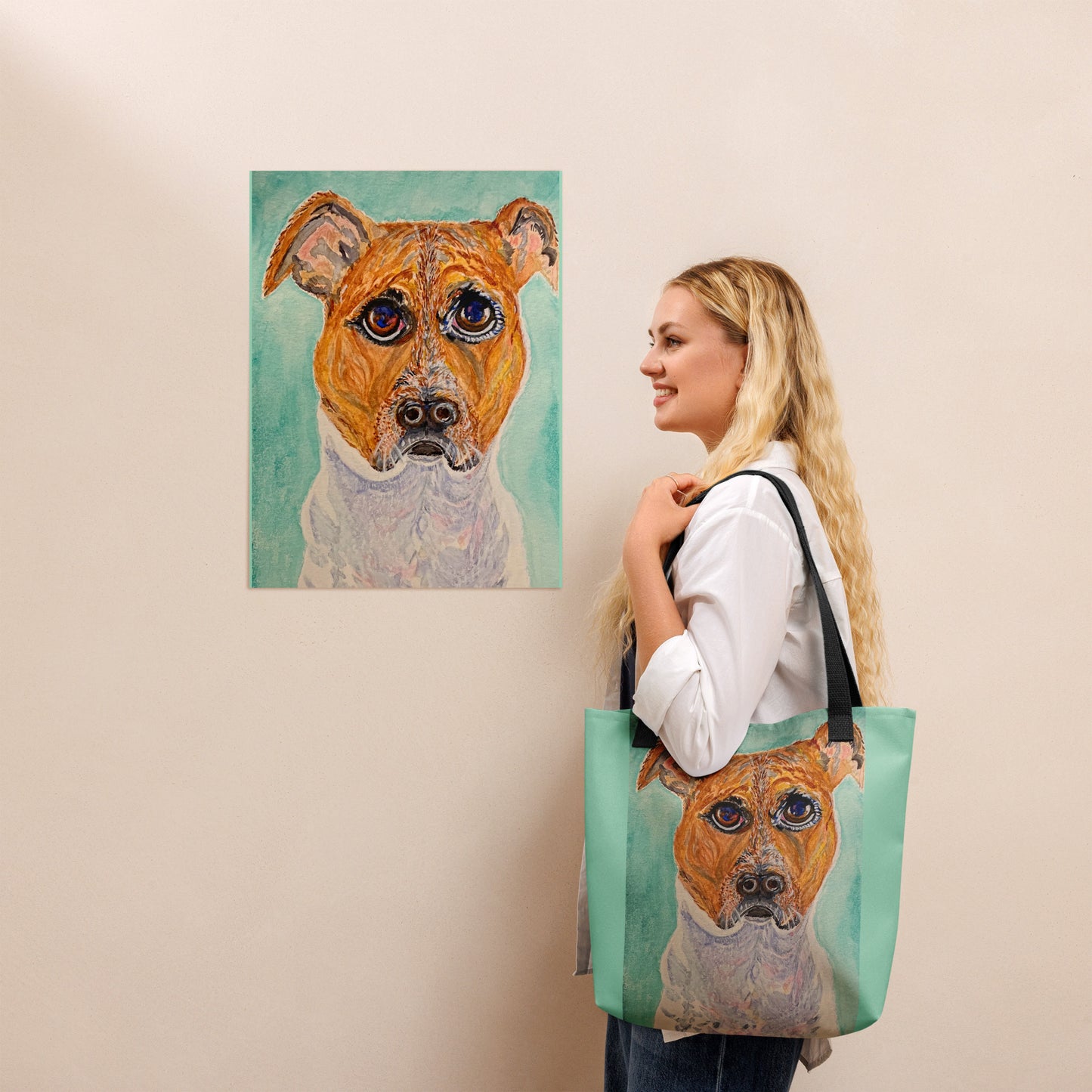 Woman holding a tote bag with a dog's face design, next to a painting of a dog on a wall.