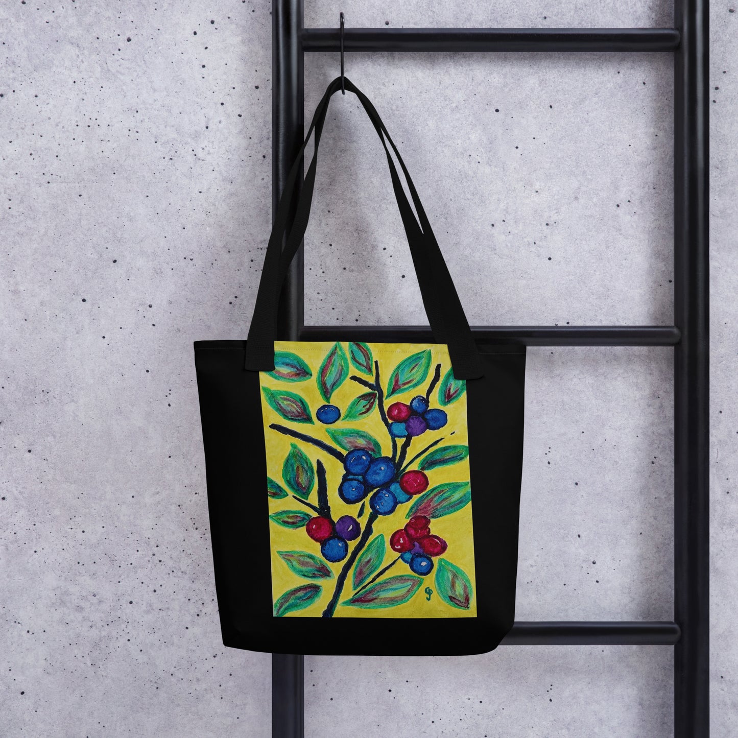 Black tote bag with a colorful berry design hanging on a black metal rack against a gray concrete wall.