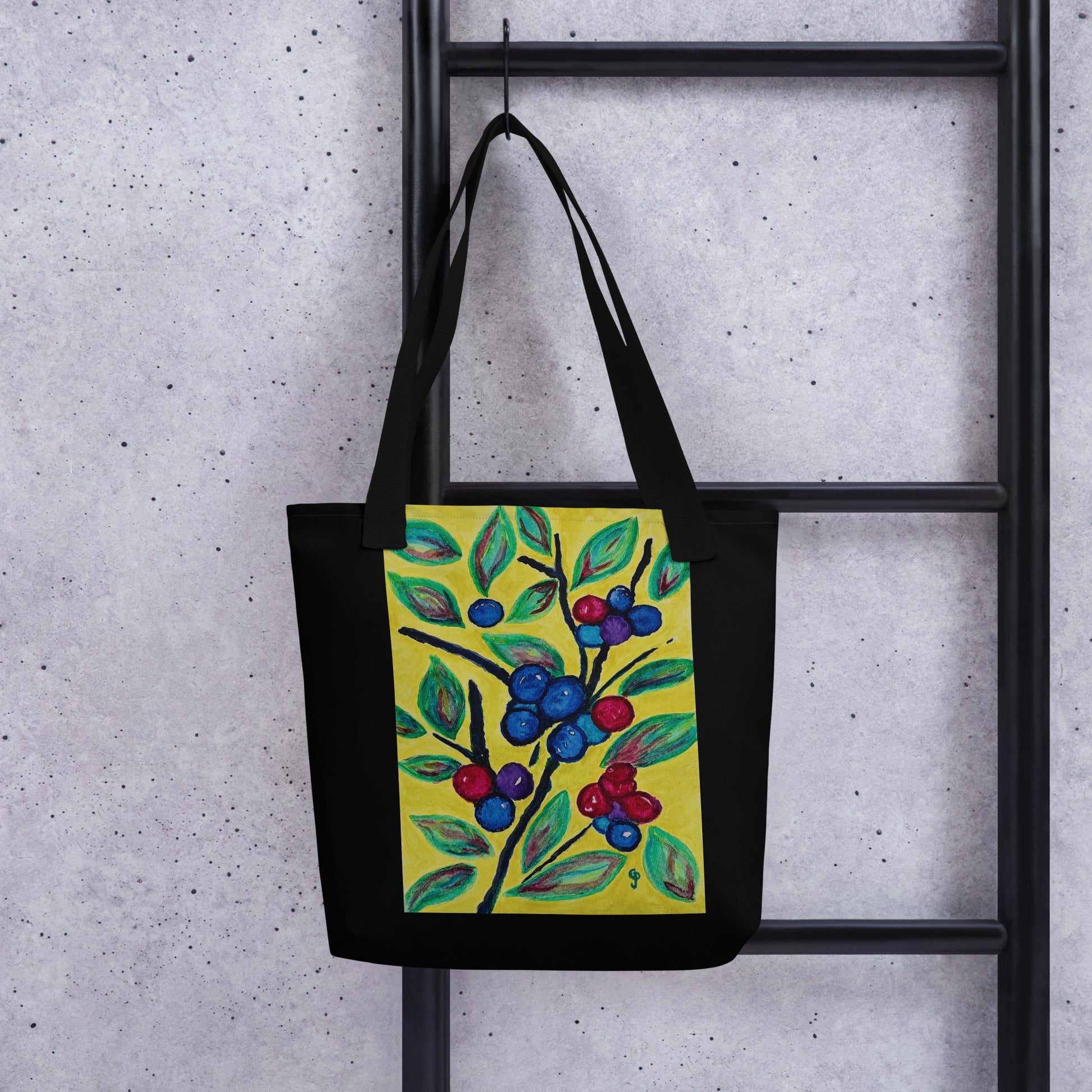 Black tote bag with a colorful berry design hanging on a black metal rack against a gray concrete wall.