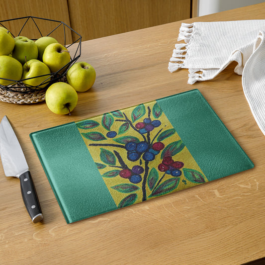 Green cutting board with fruit design on a wooden table with apples and a knife.