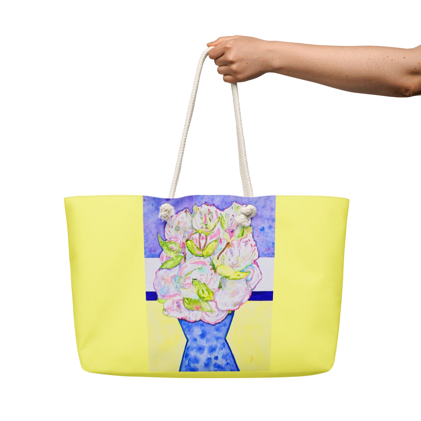 Yellow tote bag with floral design held by a hand on a white background