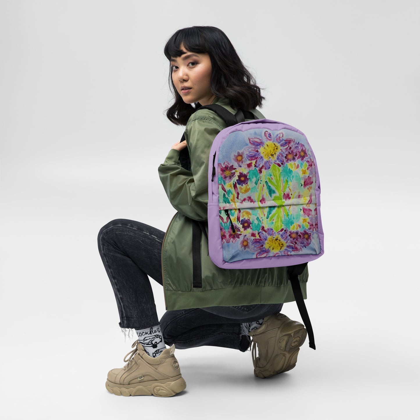 Asian person wearing a green jacket with a colorful floral backpack displaying original watercolor art