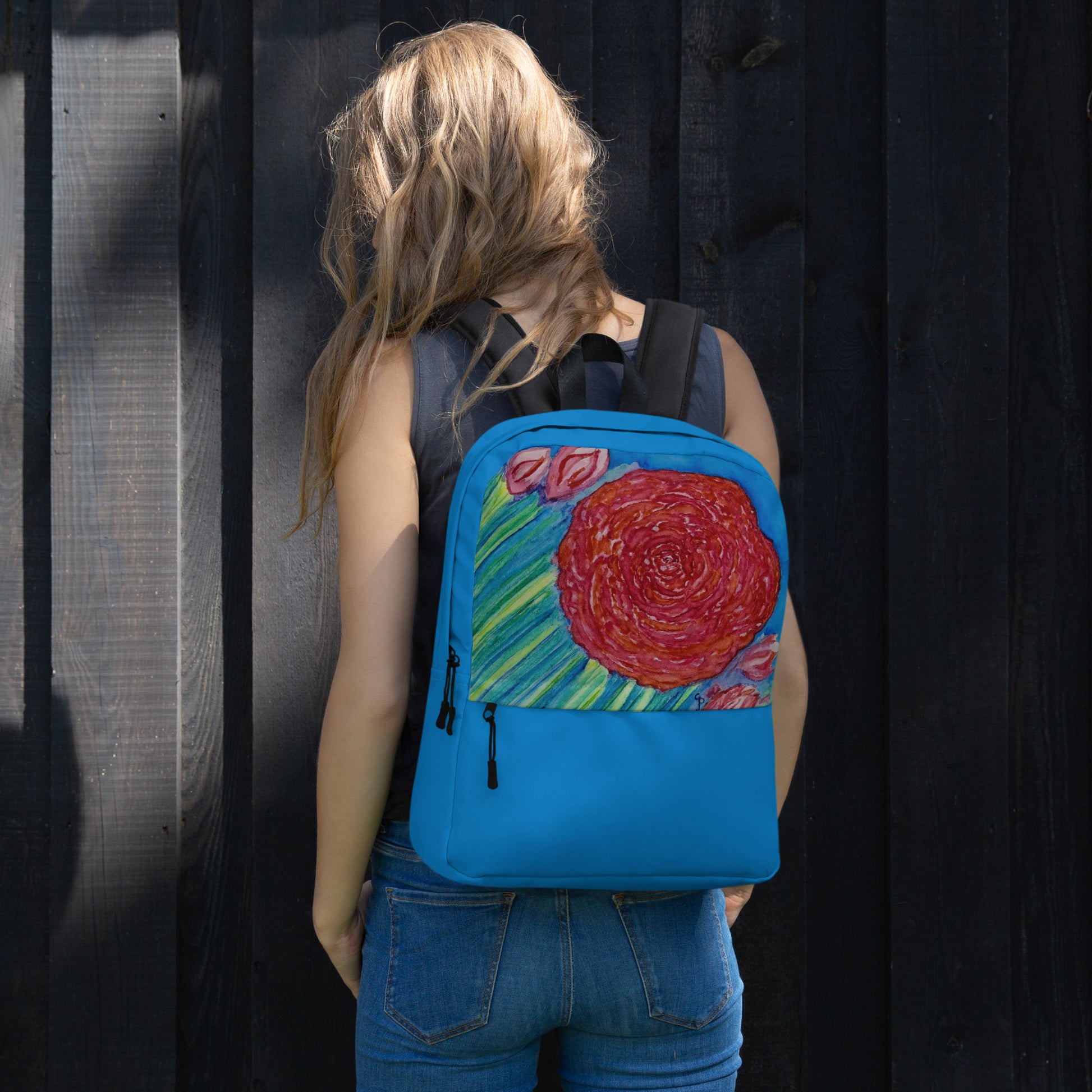 Person wearing a blue backpack with a original watercolor floral design against a dark background