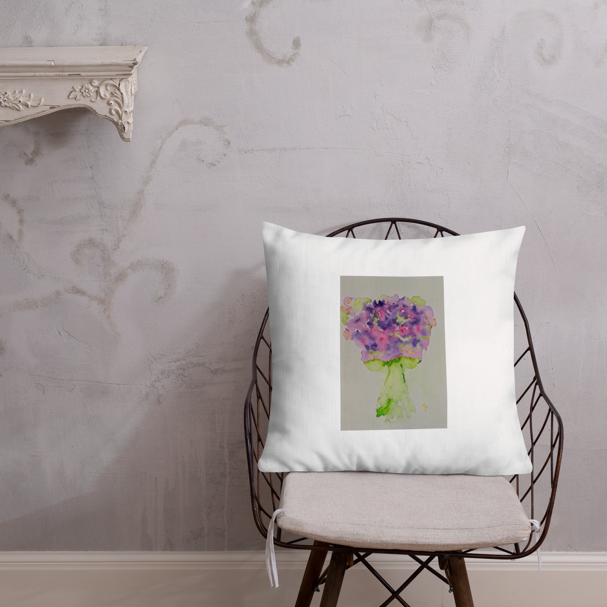 White pillow with a floral design on a chair against a textured wall.