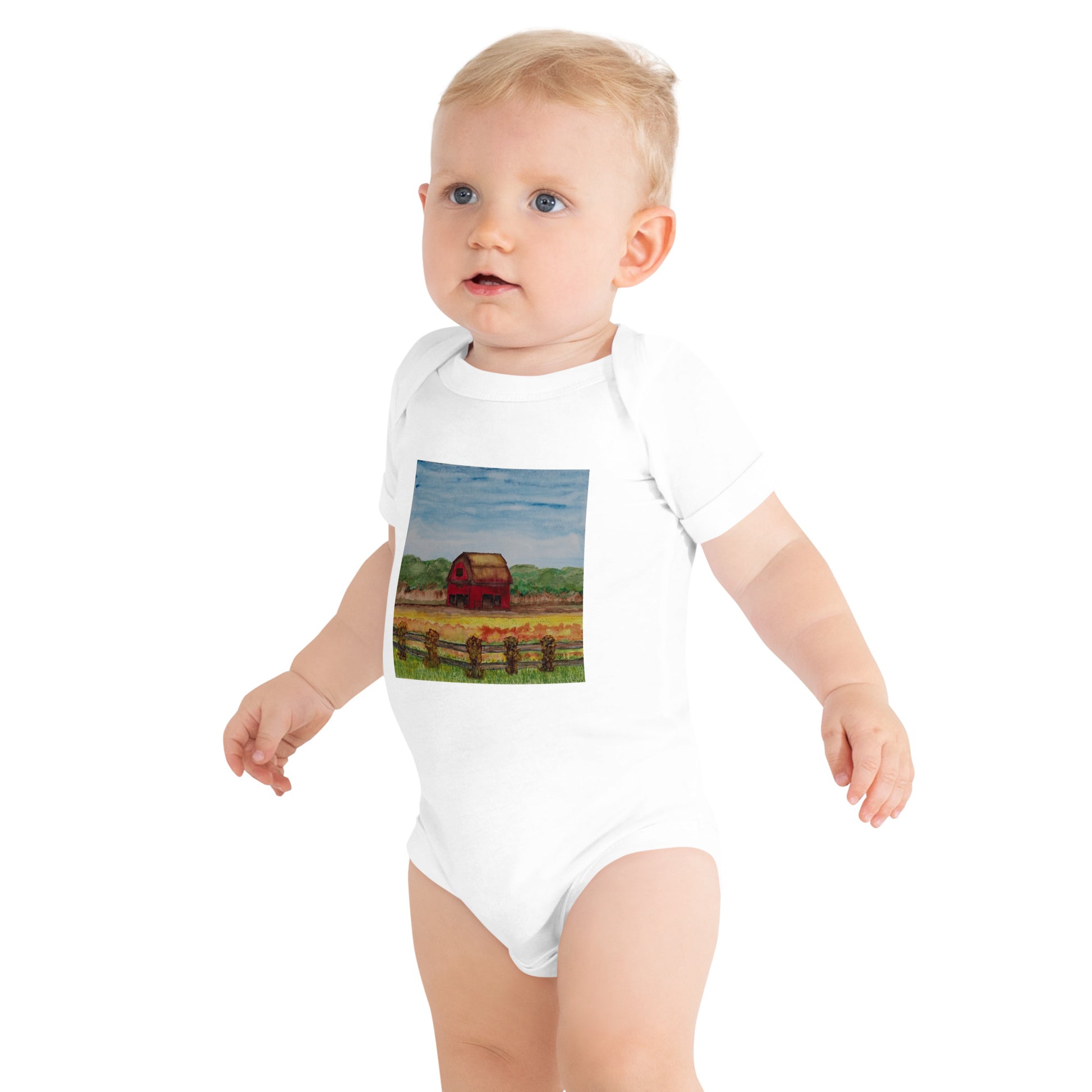 Baby wearing a white onesie with a printed design of a barn and landscape.