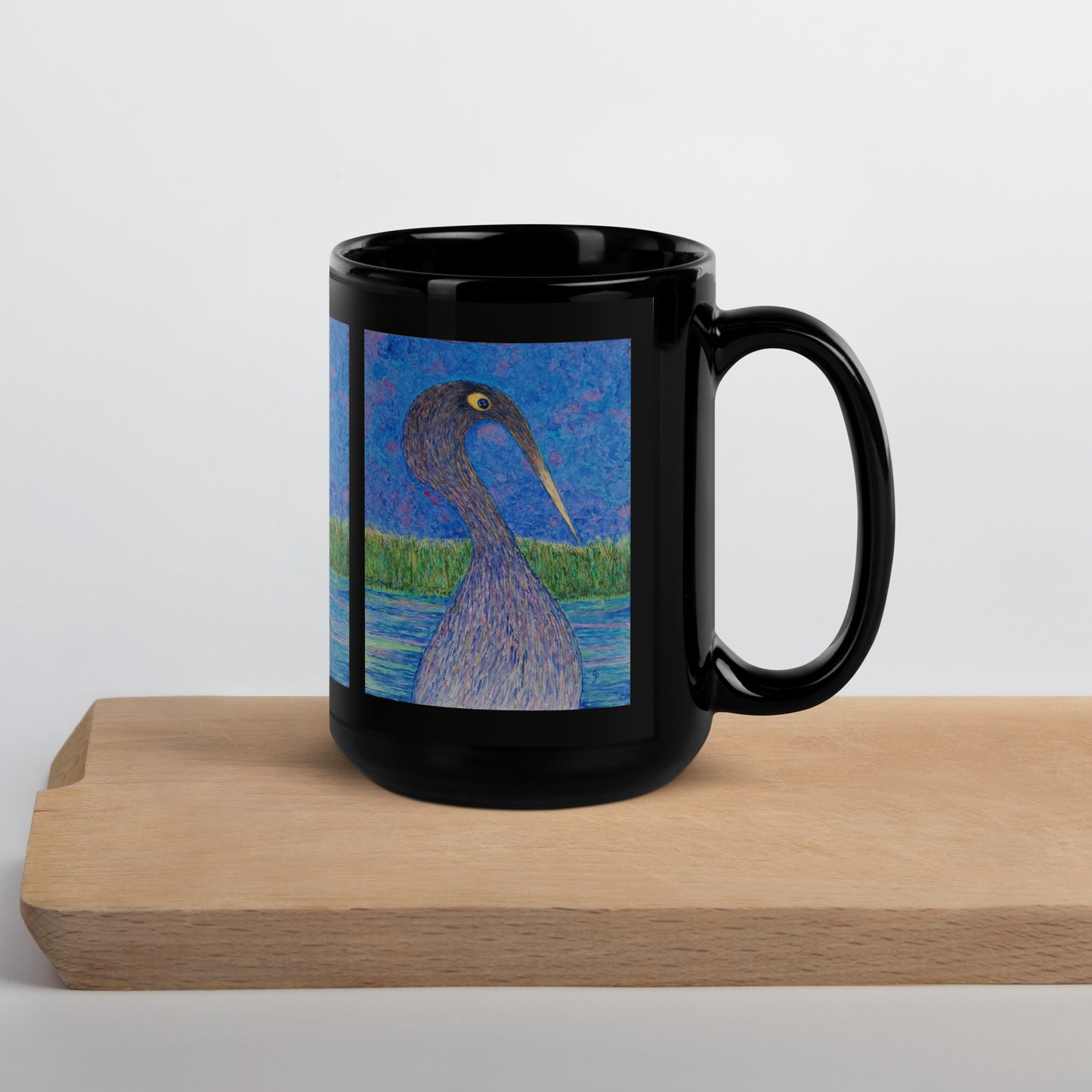 Black mug with a bird design on a wooden block against a white background