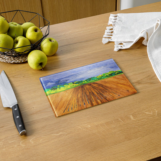 Chopping board with landscape design on a wooden table with apples and a knife.