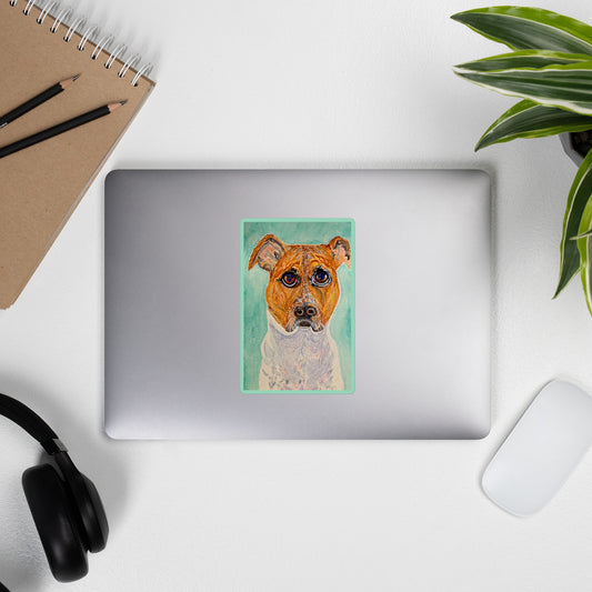 Laptop with a dog sticker on a white surface with a notebook, pencils, headphones, and a plant.