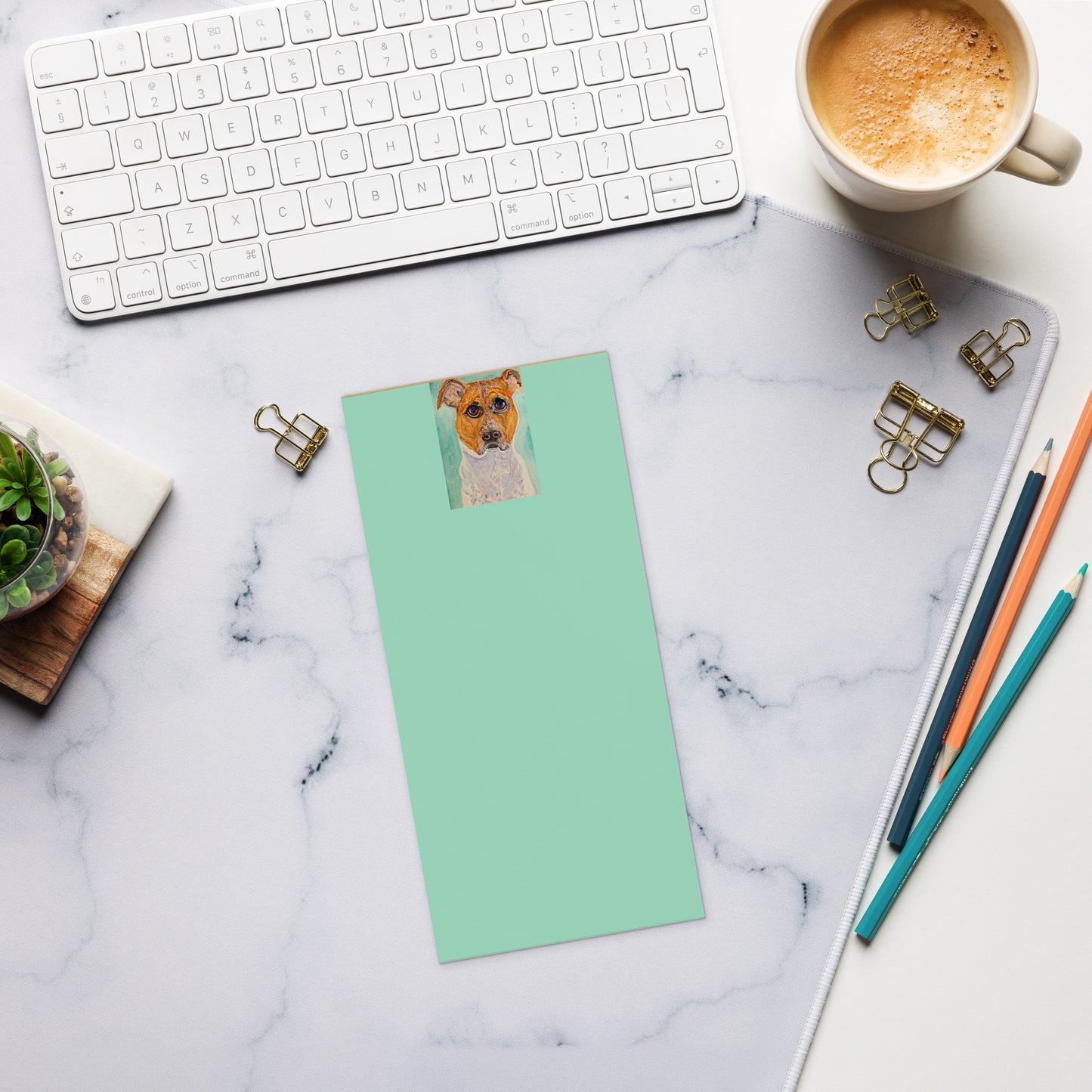 Desk setup with a keyboard, mug, stationery items, and a green notepad with a dog photo.